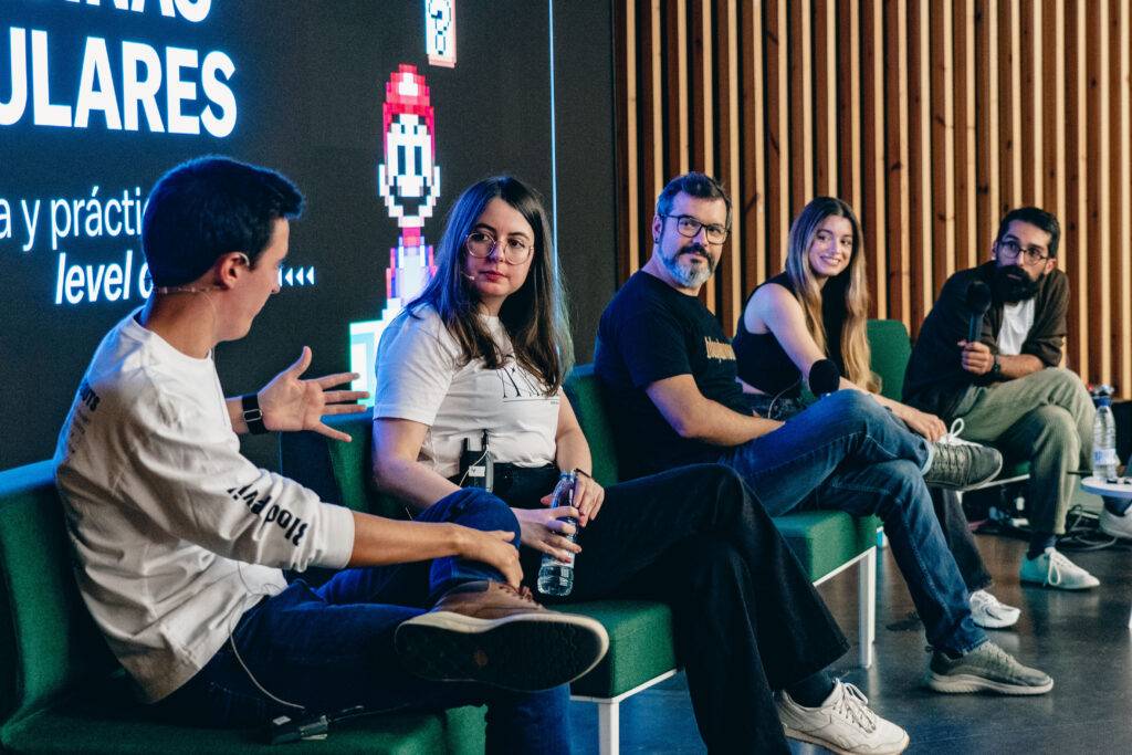 Un panel de discusión con cinco personas sentadas en un escenario, hablando sobre temas relacionados con los videojuegos.