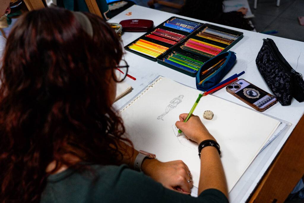 Una persona dibuja en una hoja de papel mientras está rodeada de útiles de arte.