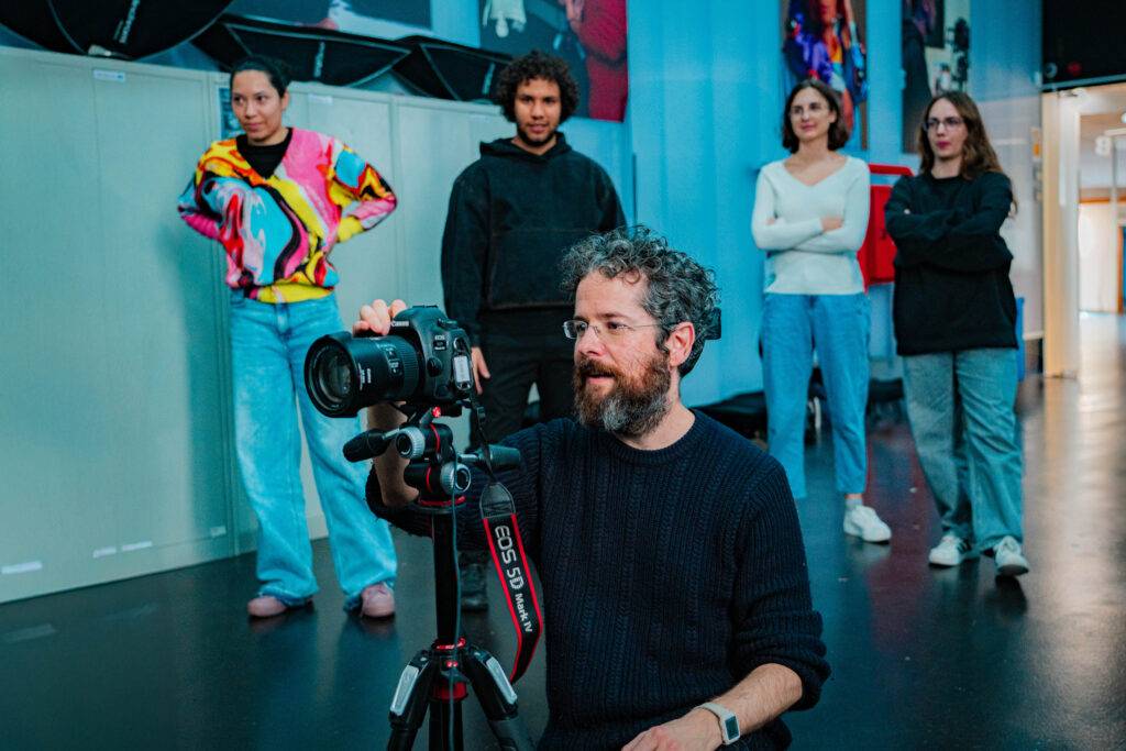 Un grupo de personas observan a un fotógrafo mientras ajusta su cámara en un estudio.