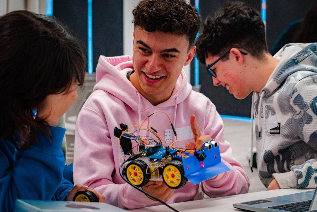 Un grupo de jóvenes se divierte mientras observan y manipulan un robot en una mesa.