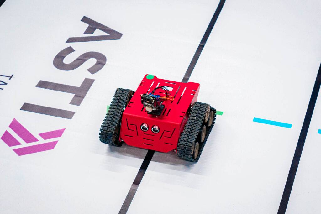Un robot de color rojo se encuentra en una pista con marcas distintivas.