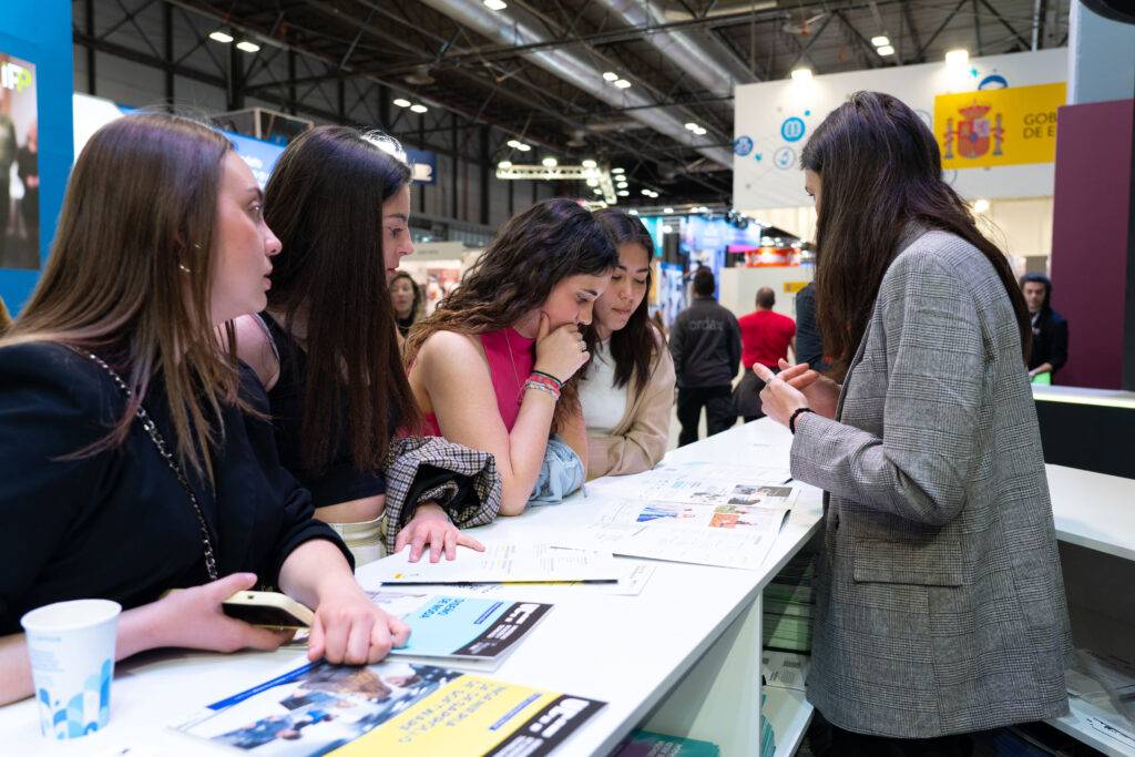 Un grupo de cinco mujeres observa atentamente unos documentos mientras conversan en un evento.