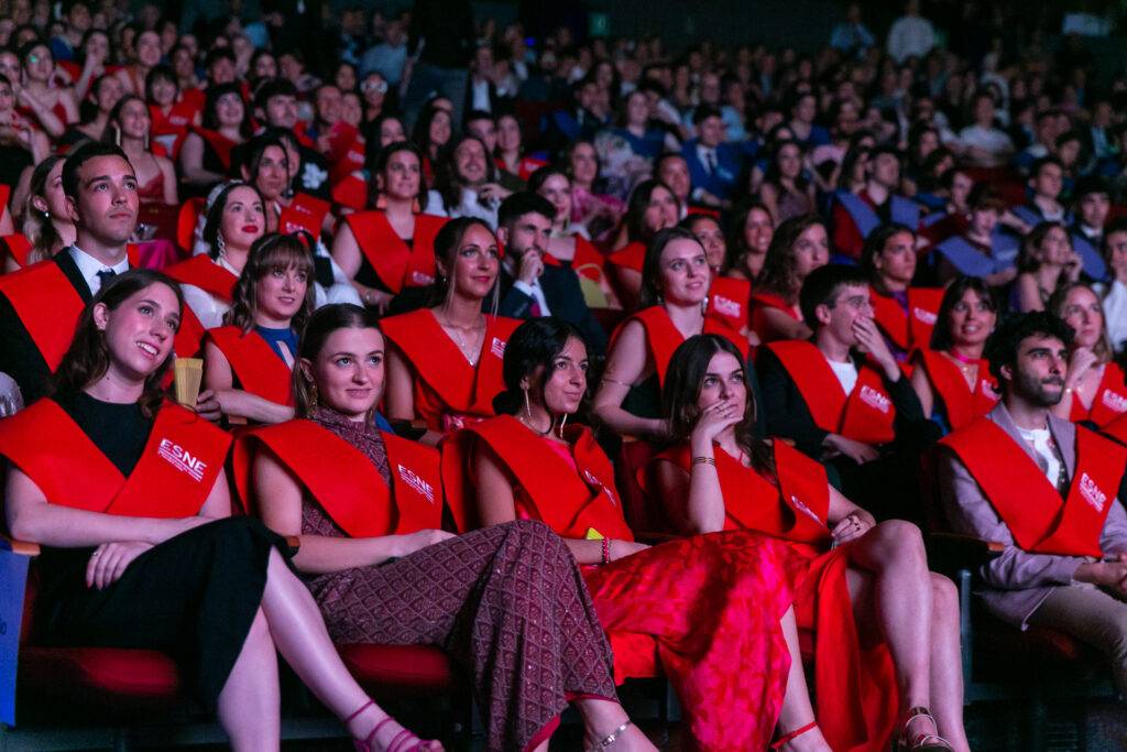 Un grupo de personas sentadas en un auditorio, vistiendo togas de graduación rojas.