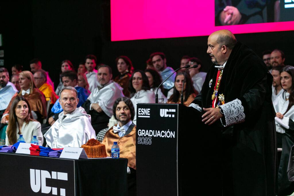 Ceremonia de graduación con un orador y varios asistentes en el escenario.