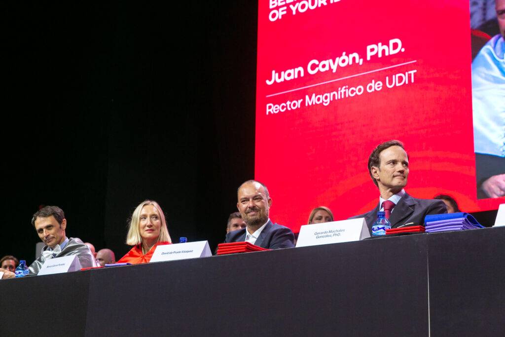 Una mesa de conferencia con varios oradores sentados enfrente de un gran banner de presentación.