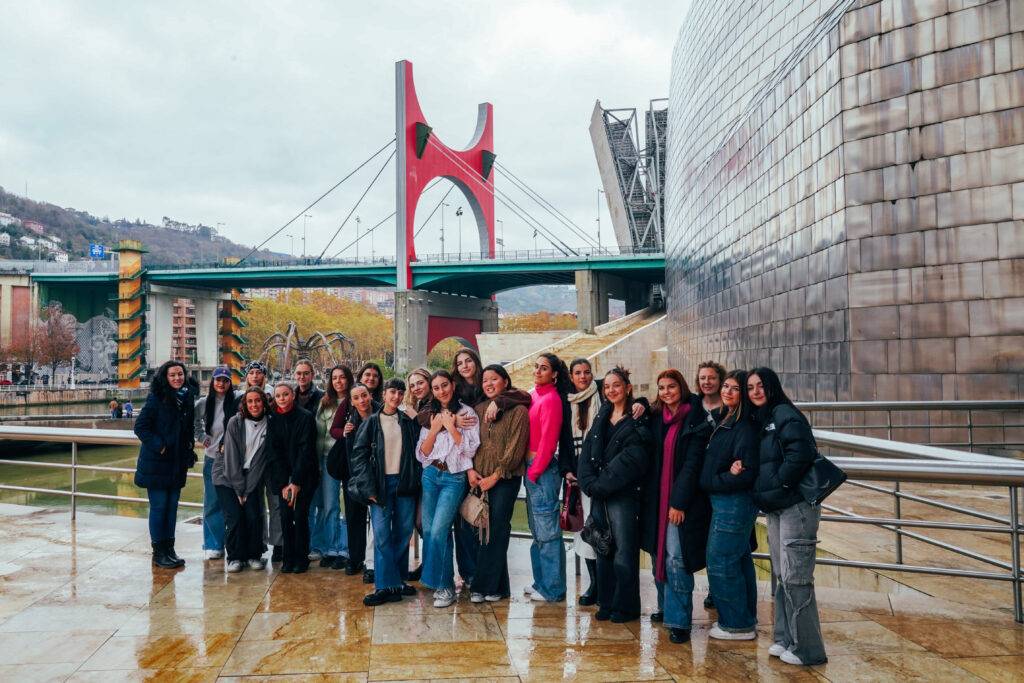 Grupo de mujeres posando frente al puente rojo sobre el río en una ciudad moderna.