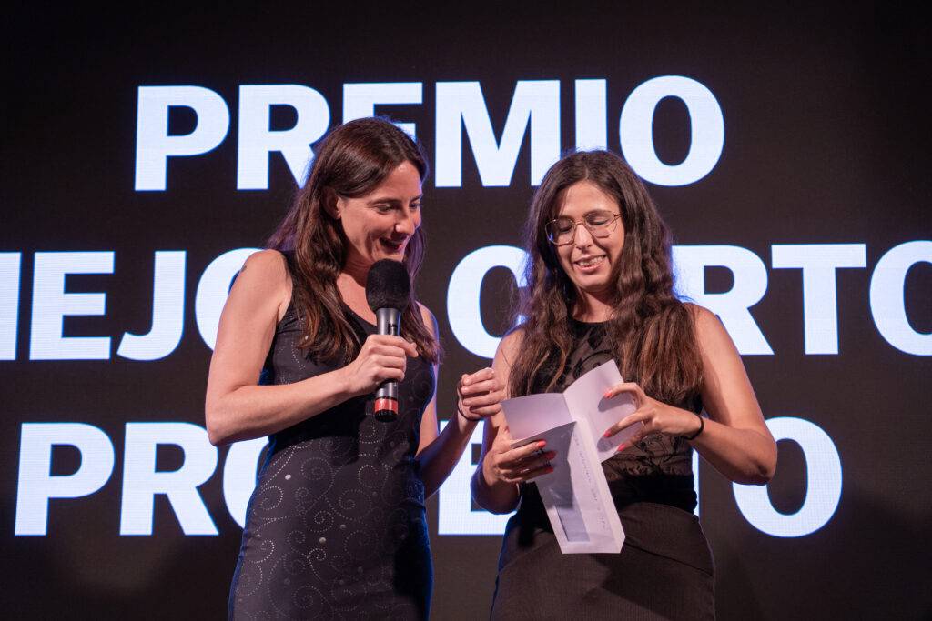 Dos mujeres en un evento entregando un premio.
