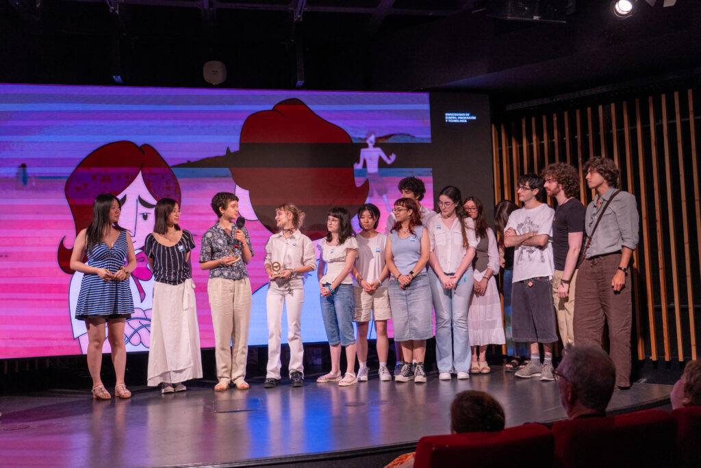 Un grupo de personas se encuentra en un escenario mientras una proyección animada se muestra detrás de ellos.