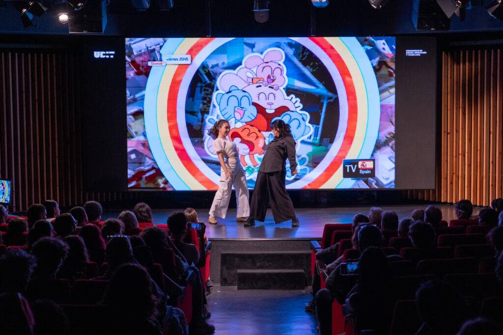 Una actuación en un escenario iluminado con una proyección colorida de un personaje animado de fondo.