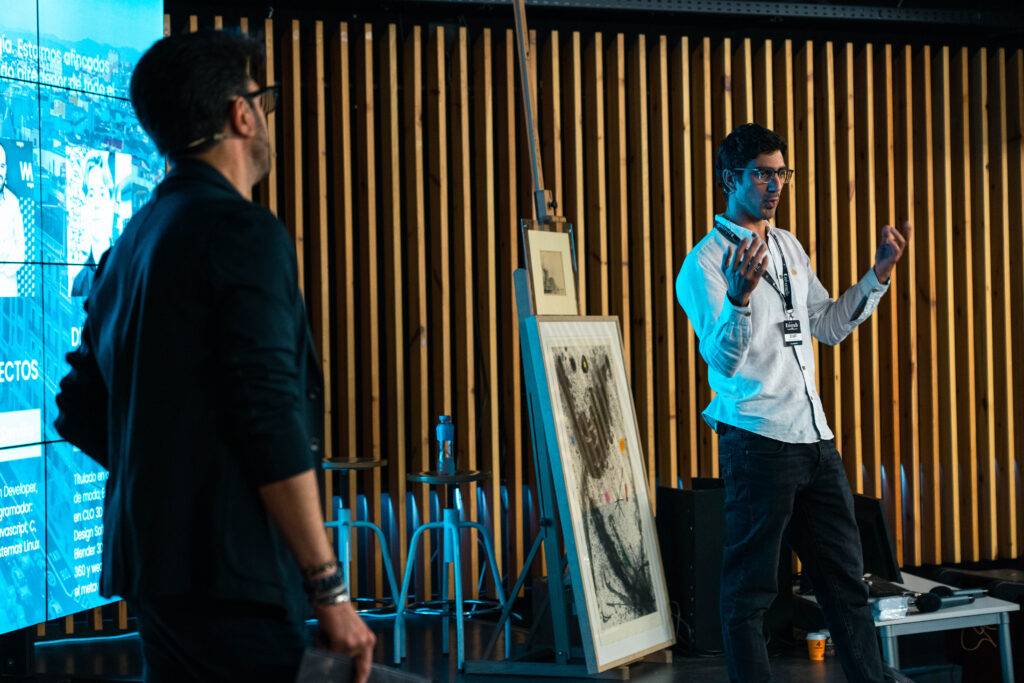 Una presentación en vivo frente a una audiencia con una obra de arte en el fondo.