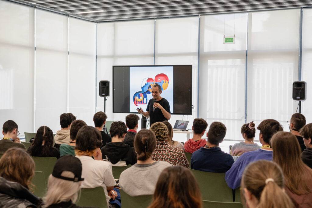 Un presentador habla frente a un grupo de jóvenes en un salón moderno.