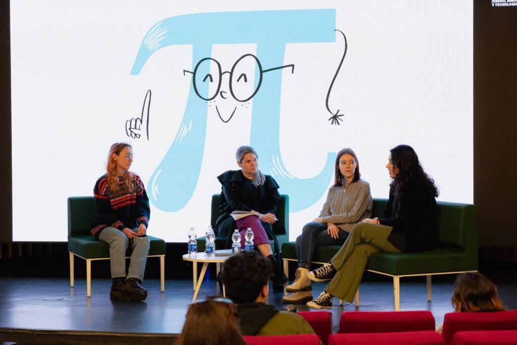 Un panel de discusión con cuatro mujeres sentadas frente a un fondo que muestra un dibujo del símbolo pi.