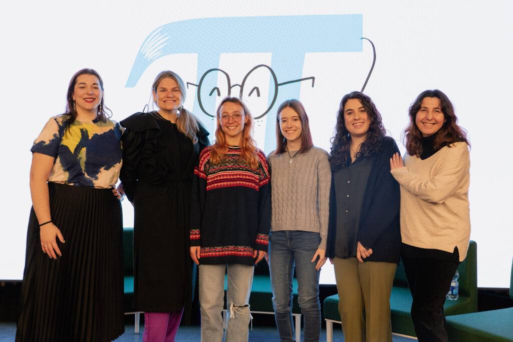 Un grupo de seis mujeres sonrientes posan juntas frente a un fondo con un diseño gráfico.