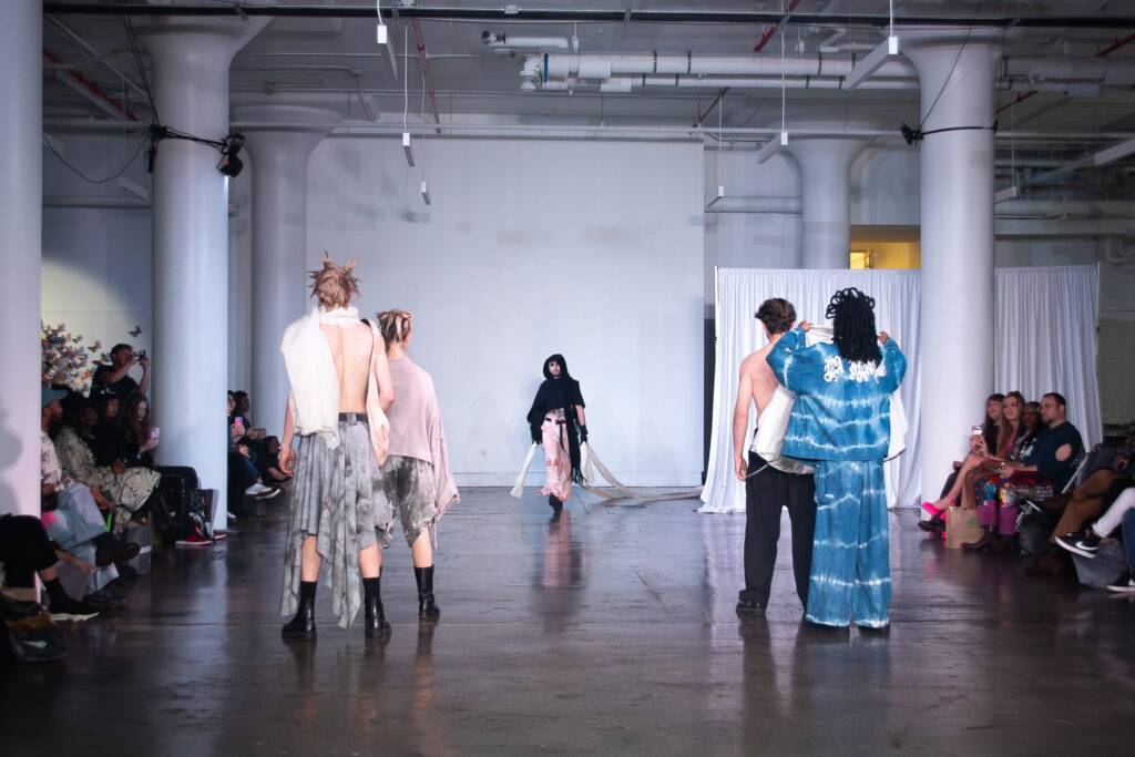 Un desfile de moda en un ambiente industrial con modelos y un público atento.