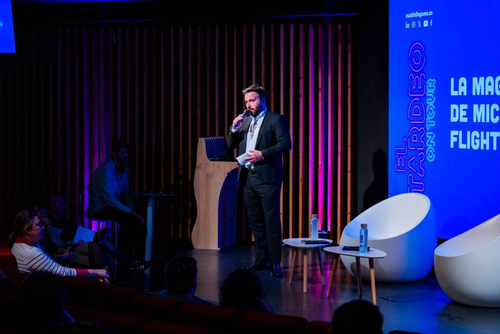 Un presentador hablando en un evento sobre tecnología frente a una audiencia sentada.
