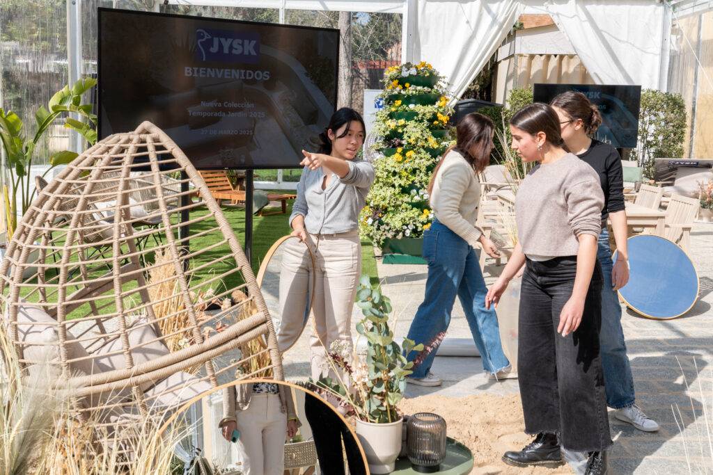 Un grupo de personas interactúa en un ambiente decorativo al aire libre, señalando y organizando elementos de diseño.