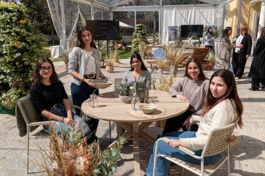 Un grupo de cinco mujeres sentadas alrededor de una mesa en un ambiente al aire libre con decoración floral.