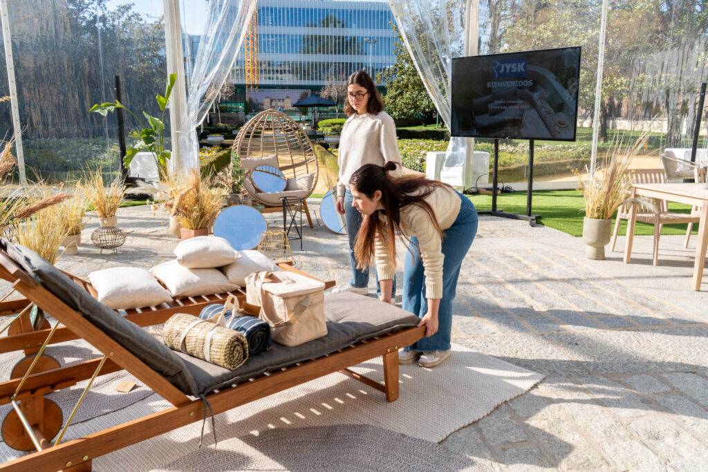 Dos mujeres están organizando una zona de descanso al aire libre con muebles y decoraciones.