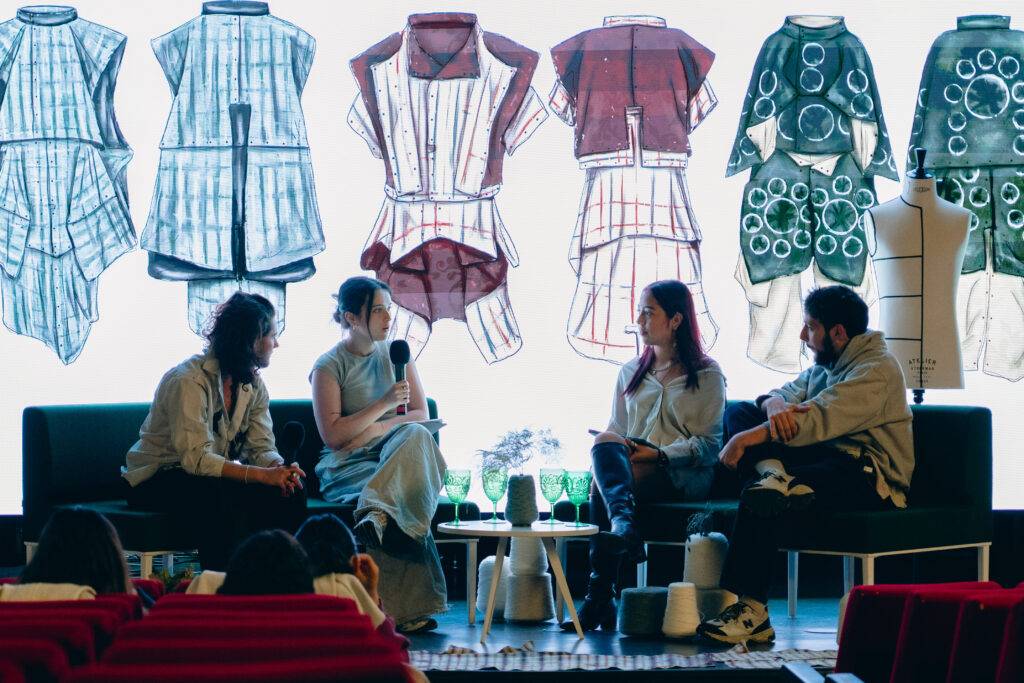 Un grupo de personas discute frente a un fondo de diseños de ropa en un evento creativo.