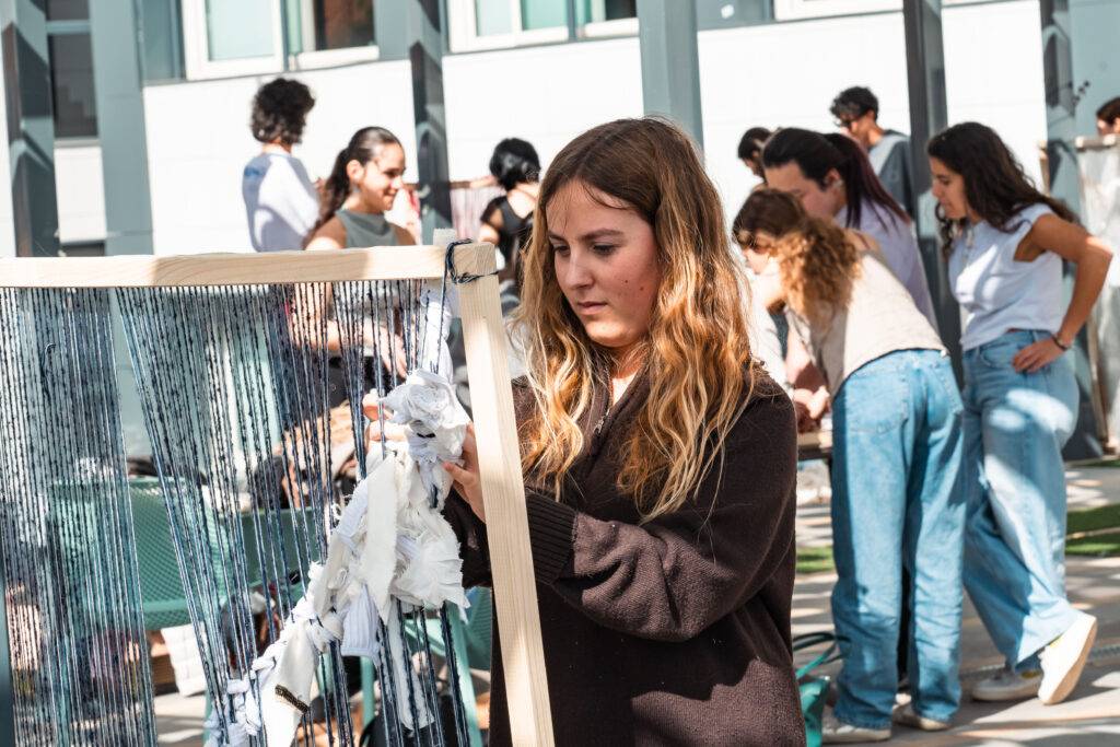 Una joven trabaja en una actividad creativa mientras otras personas participan en el fondo.
