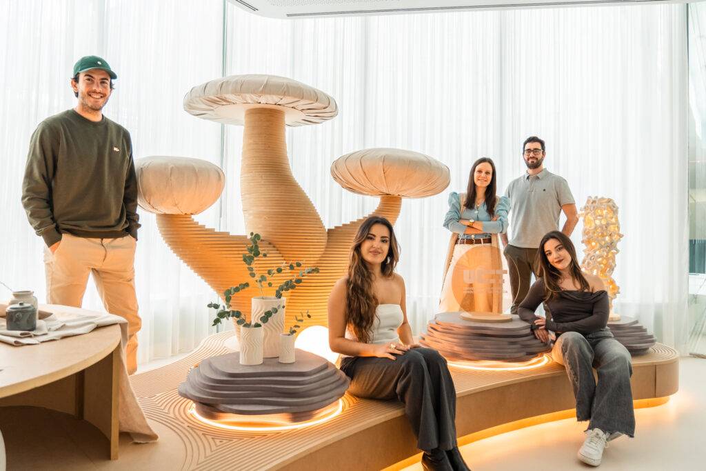Un grupo de seis personas posando en un espacio moderno y luminoso con elementos decorativos que simulan hongos y plantas.