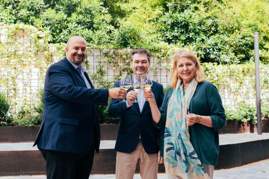 Tres personas levantan copas en un brindis al aire libre.