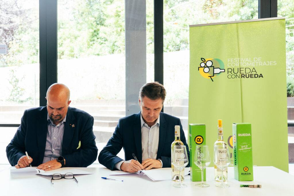 Dos hombres firman documentos en un evento relacionado con el vino en Rueda.