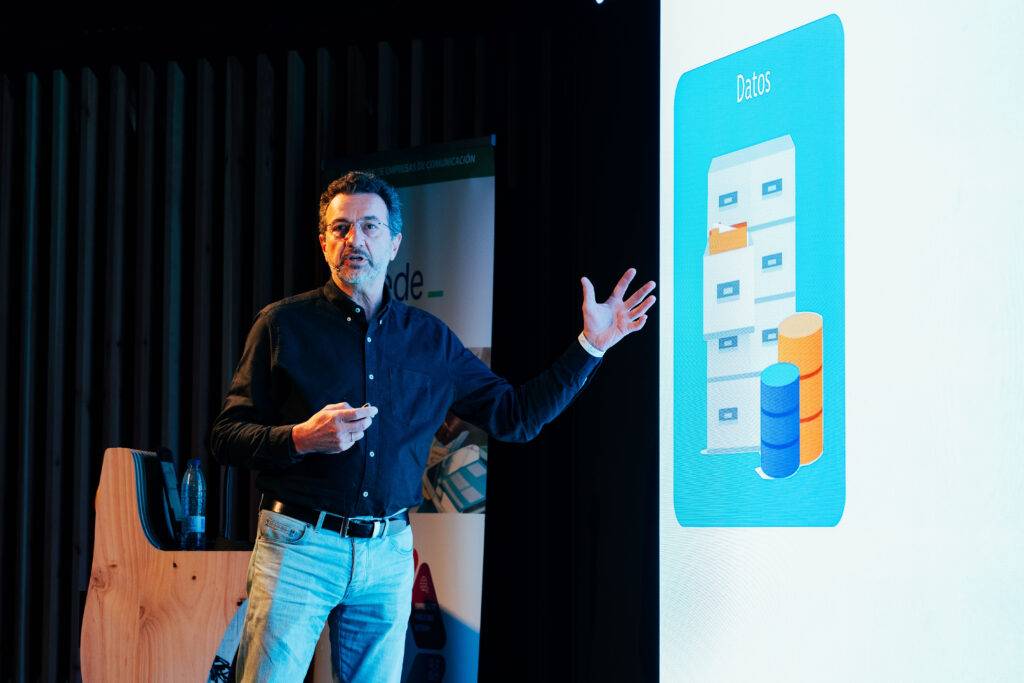 Un presentador está hablando sobre datos frente a una pantalla con gráficos.