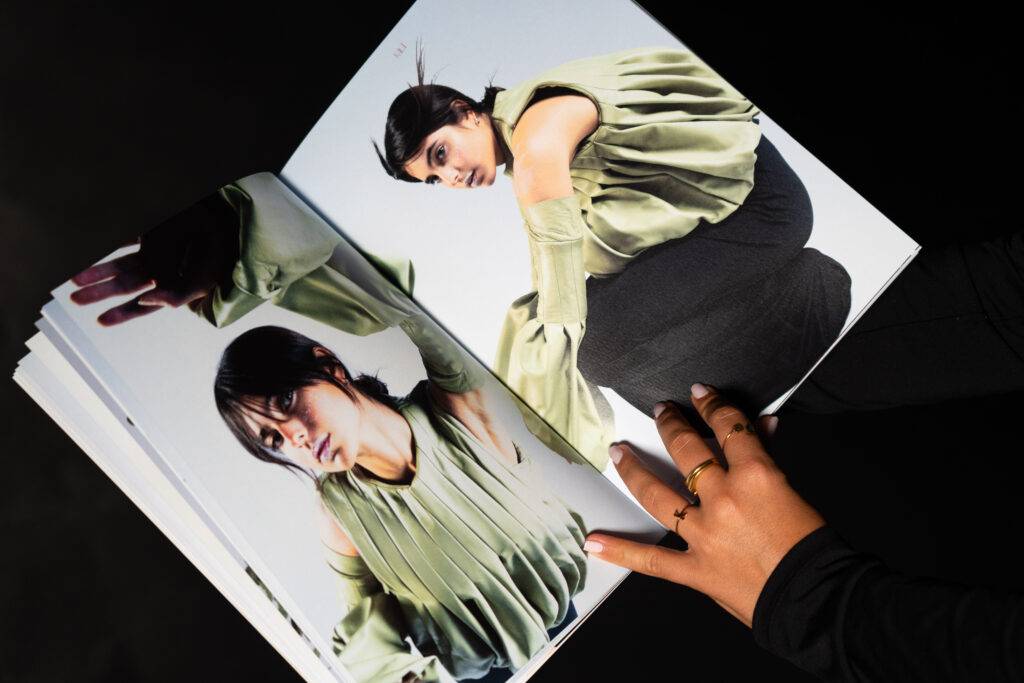 Una persona sostiene un libro de moda donde se ven dos imágenes de una modelo con un atuendo verde.