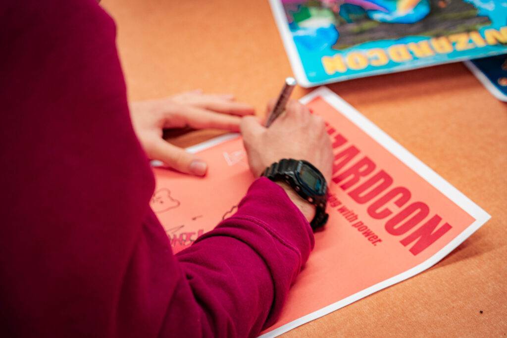 Una persona está escribiendo en un papel que dice 'HARDCON'.