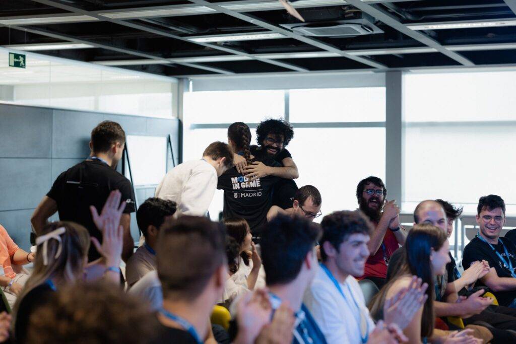 Un grupo de personas aplaudiendo mientras dos individuos se abrazan en un evento.