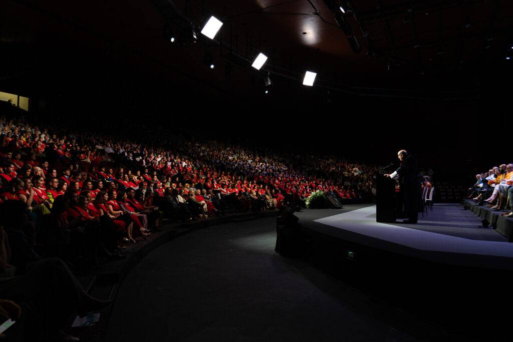 Un orador se dirige a una multitud numerosa en un evento en un auditorio.