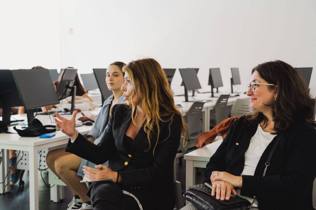 Un grupo de mujeres se encuentra en un aula con computadoras, mientras una de ellas habla animadamente.