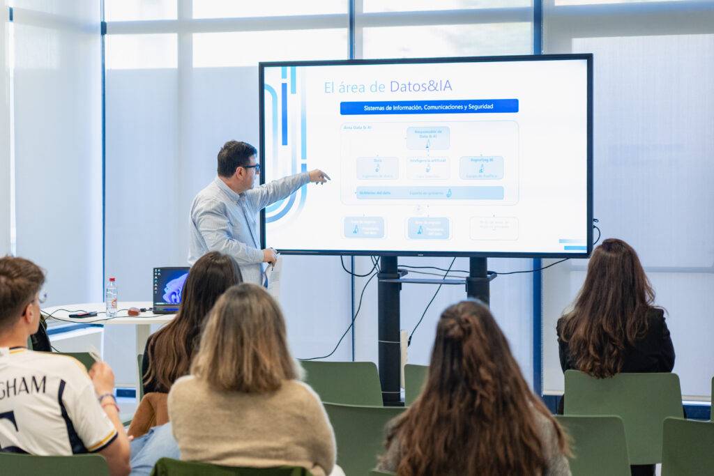 Un presentador explica un tema sobre datos e inteligencia artificial frente a una audiencia en una sala moderna.
