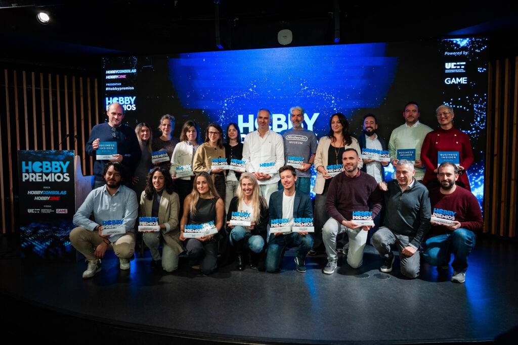 Un grupo de personas posando en un evento con premios en un escenario ilustrativo.