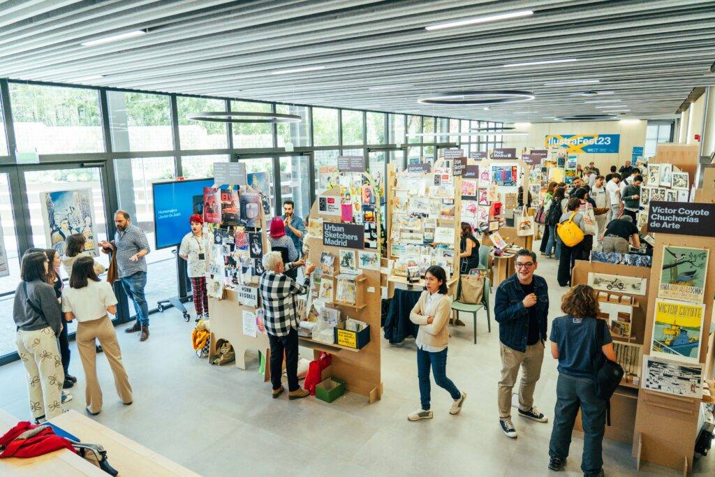 Una feria con varias personas interactuando entre estands repletos de publicaciones y arte.