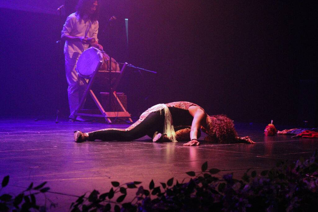 Una bailarina se desploma sobre el escenario mientras un músico toca un tambor.