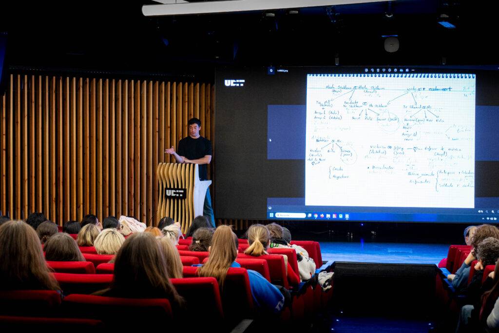 Un presentador expone en un auditorio mientras una proyección de notas se visualiza en pantalla.
