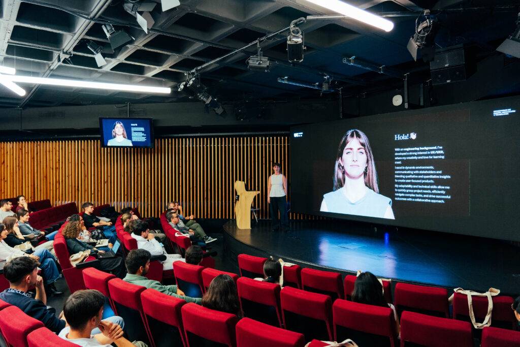 Un grupo de personas asiste a una presentación en un auditorio moderno con pantallas grandes.