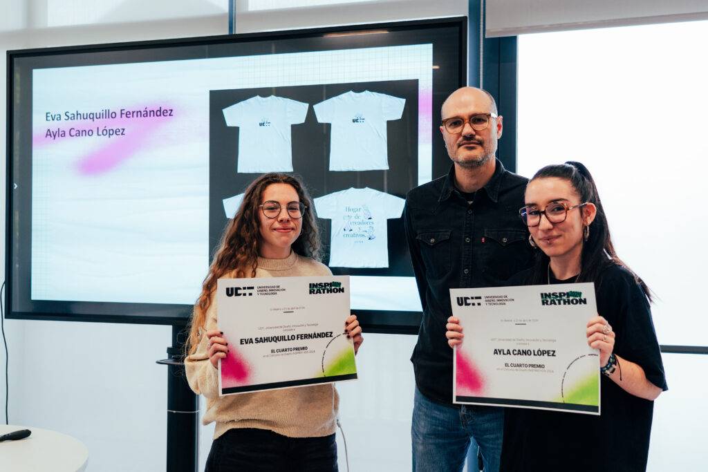 Un grupo de tres personas sonríen mientras sostienen certificados frente a una pantalla que muestra camisetas.
