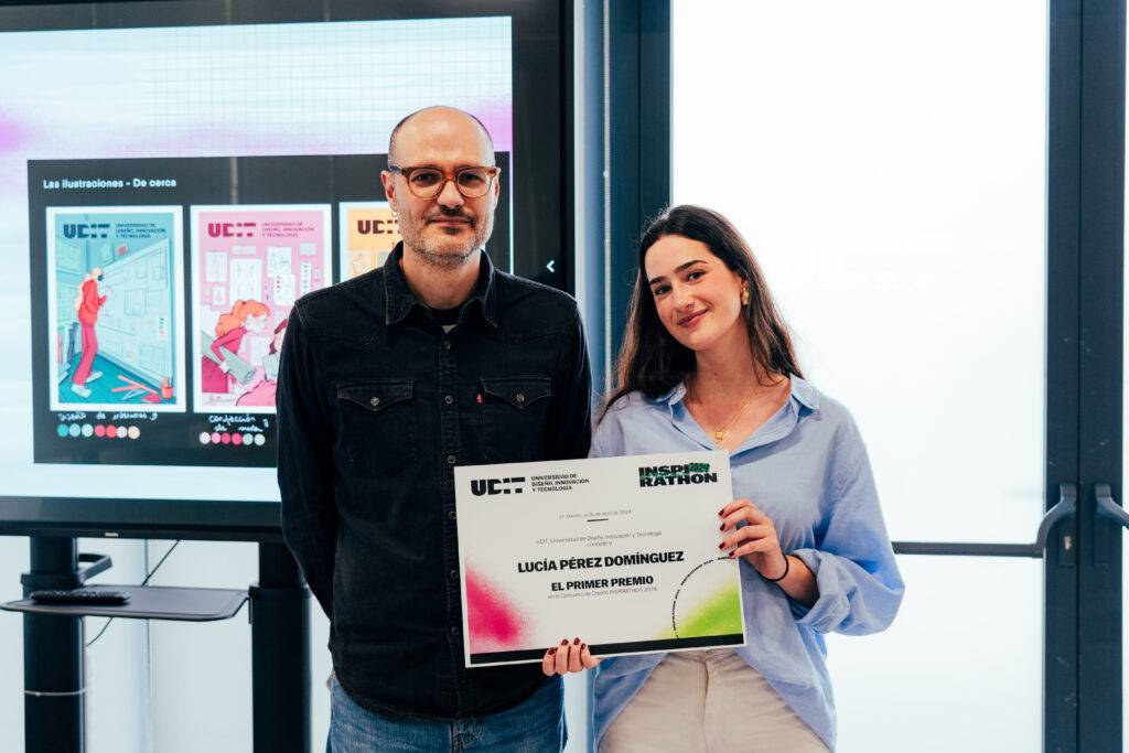 Un hombre y una mujer posan juntos sosteniendo un premio en un evento con pantallas de fondo.