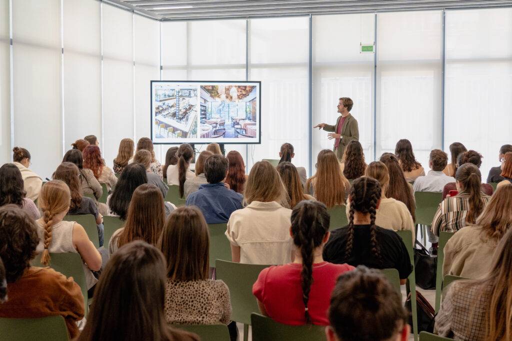 Una presentación en un salón lleno de personas que observan atentamente a un ponente frente a una pantalla.