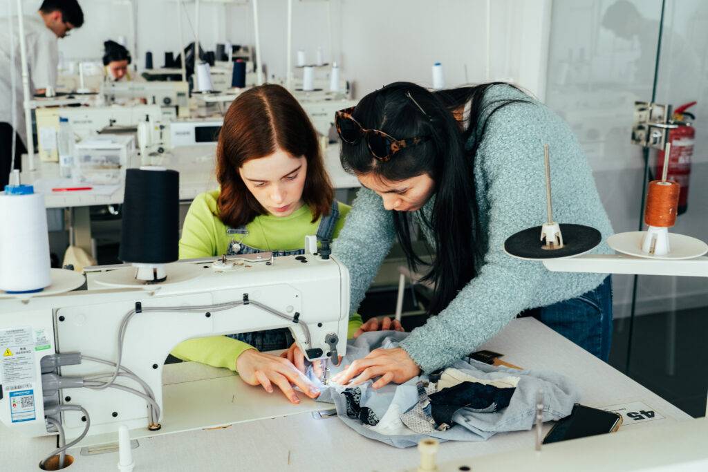 Dos jóvenes están trabajando juntas en una máquina de coser en un entorno de taller.