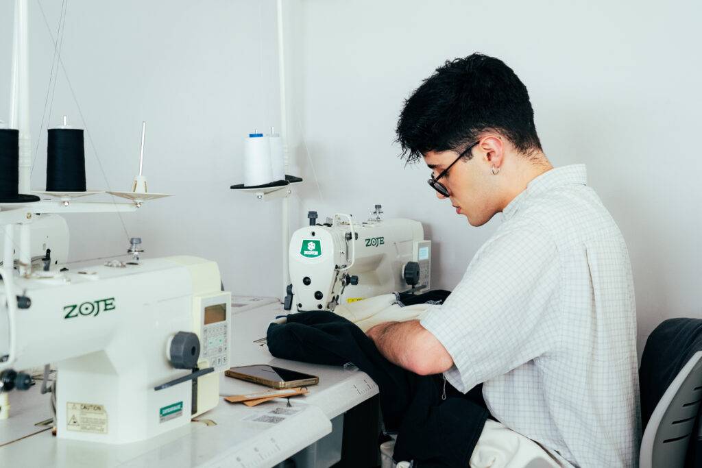 Un joven está cosiendo en una máquina de coser en un taller.