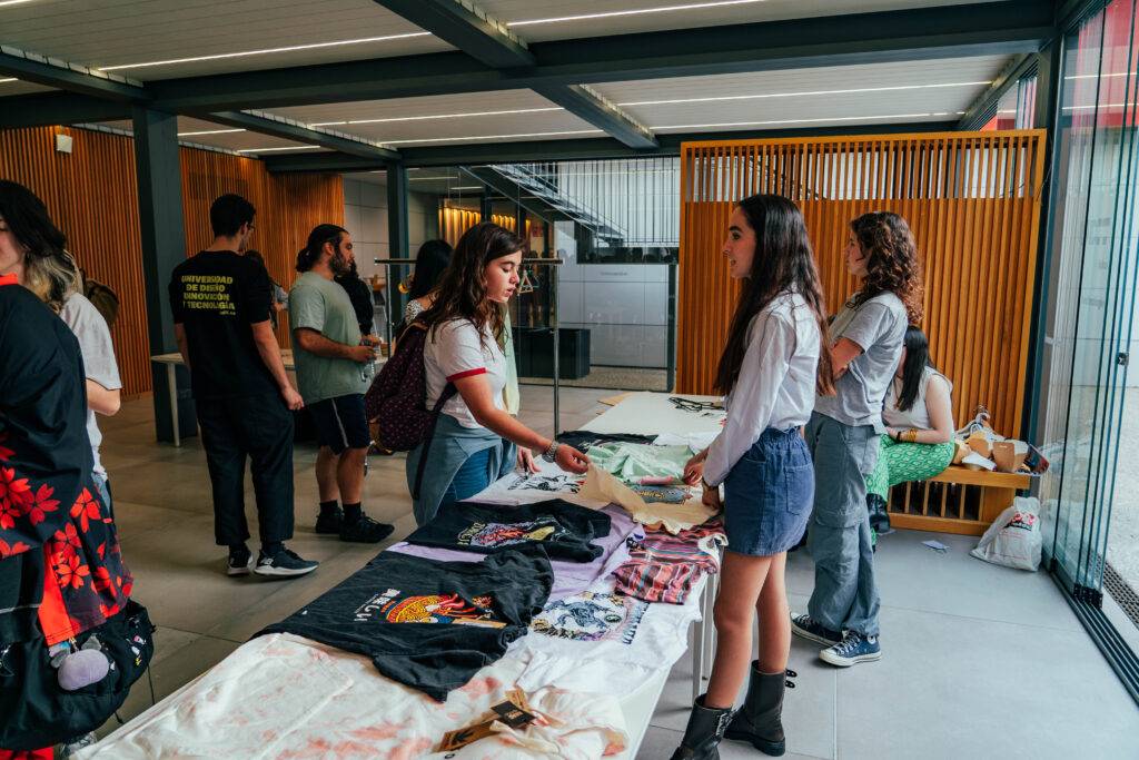 Un grupo de personas interactúa mientras revisan ropa en una venta al aire libre.
