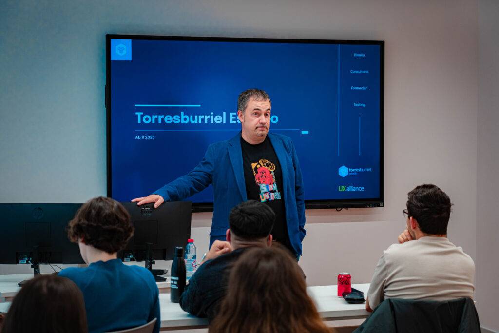 Un presentador habla frente a una audiencia en una sala de clases moderna.
