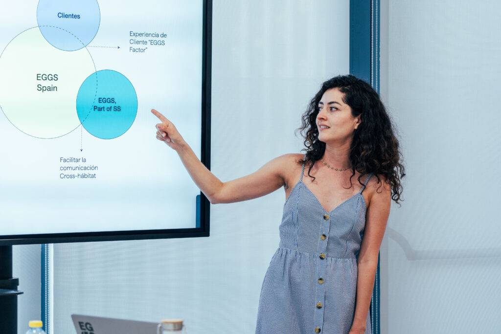 Una mujer presenta gráficos en una reunión, señalando a una pantalla interactiva.
