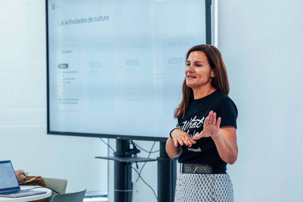 Una mujer habla frente a una pantalla sobre actividades culturales.
