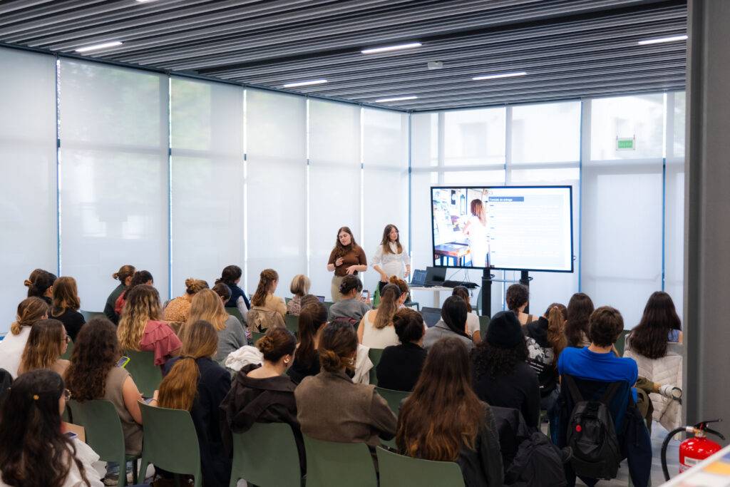 Una presentación en un aula con un grupo de personas sentadas y dos oradoras en el frente.