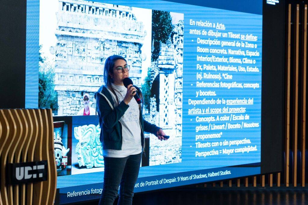 Una presentadora habla sobre el arte y los conceptos de diseño gráfico, con una imagen de fondo que muestra arquitectura antigua.